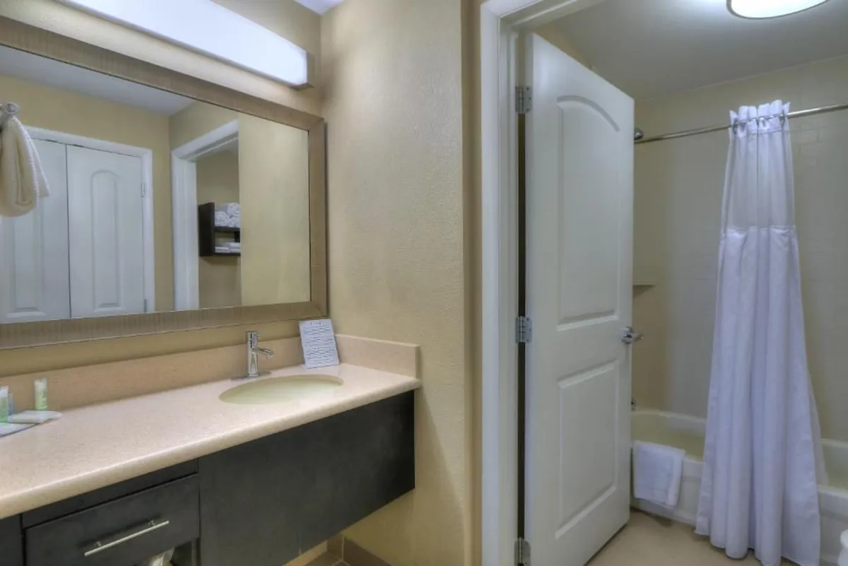 The image shows a bright, modern bathroom featuring a spacious vanity with a large mirror and a sleek shower area. The clean, well-organized layout and inviting lighting create a sense of comfort and relaxation.