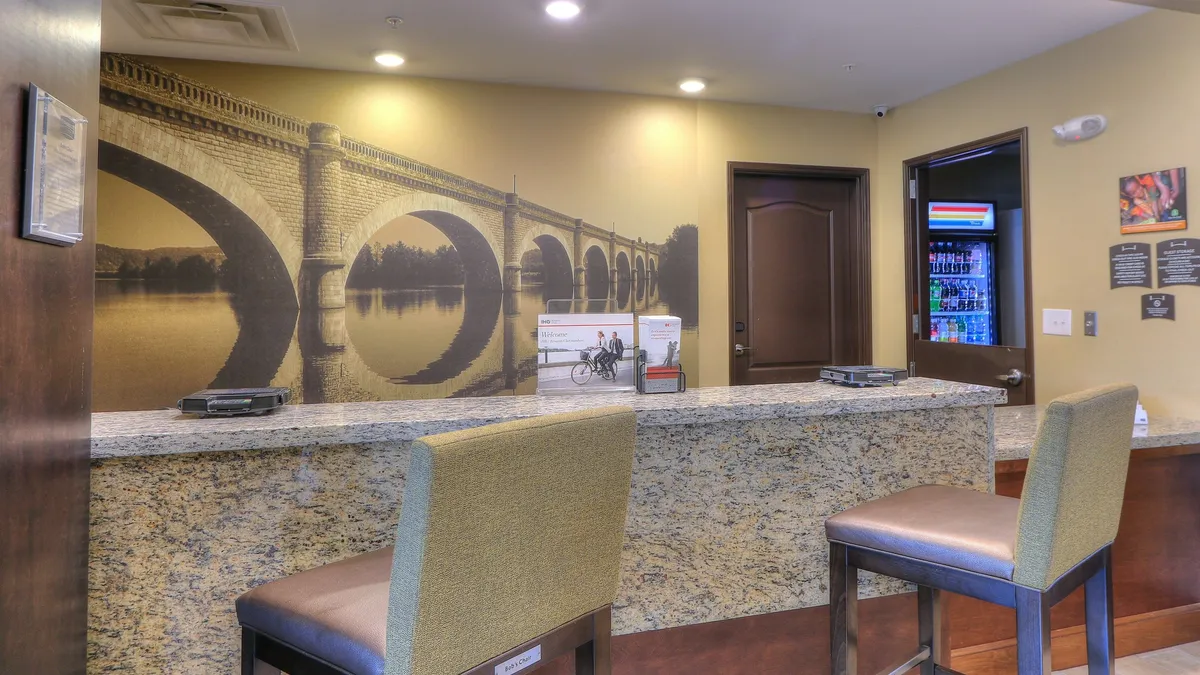 This image shows a modern, inviting reception area with a granite countertop, a striking bridge mural, seating stools, and soft lighting. The space is clean and well-organized, creating a sense of comfort and professionalism.
