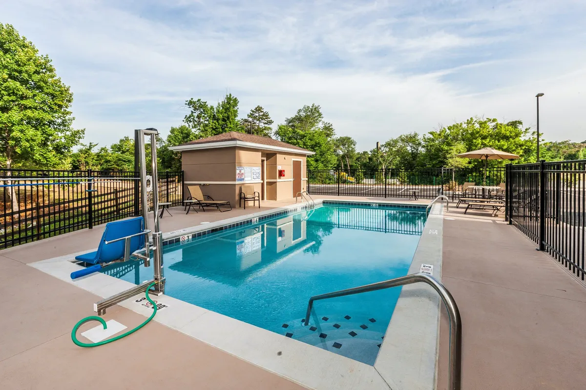 This exterior shot features the inviting outdoor heated swimming pool surrounded by lounge chairs and a poolside lift, with a pool house visible in the background. The environment is set up for both relaxation and social gatherings, emphasizing the pool's role as a communal hub during the warmer months.